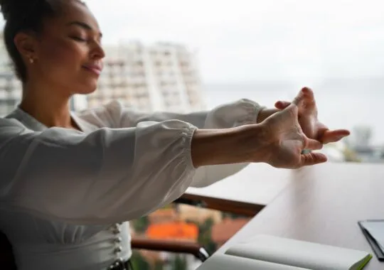 Mulher sentada em frente uma mesa esticando os braços para frente